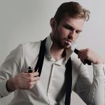 a man wearing a white dress shirt with black tie holding a vape in his hand while vaping